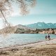 Two people walking on Queenstown Wanaka lakeshore with mountains in background.